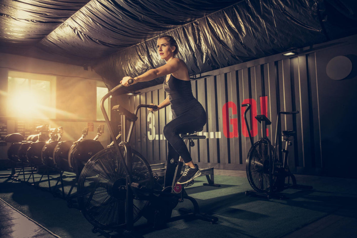Spor salonunda kondisyon bisikletinde kardiyo yapan sporcu kadın